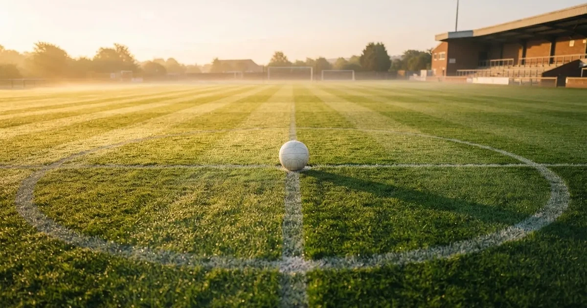 Een voetbal op de middenstip van een grasveld in het ochtendlicht