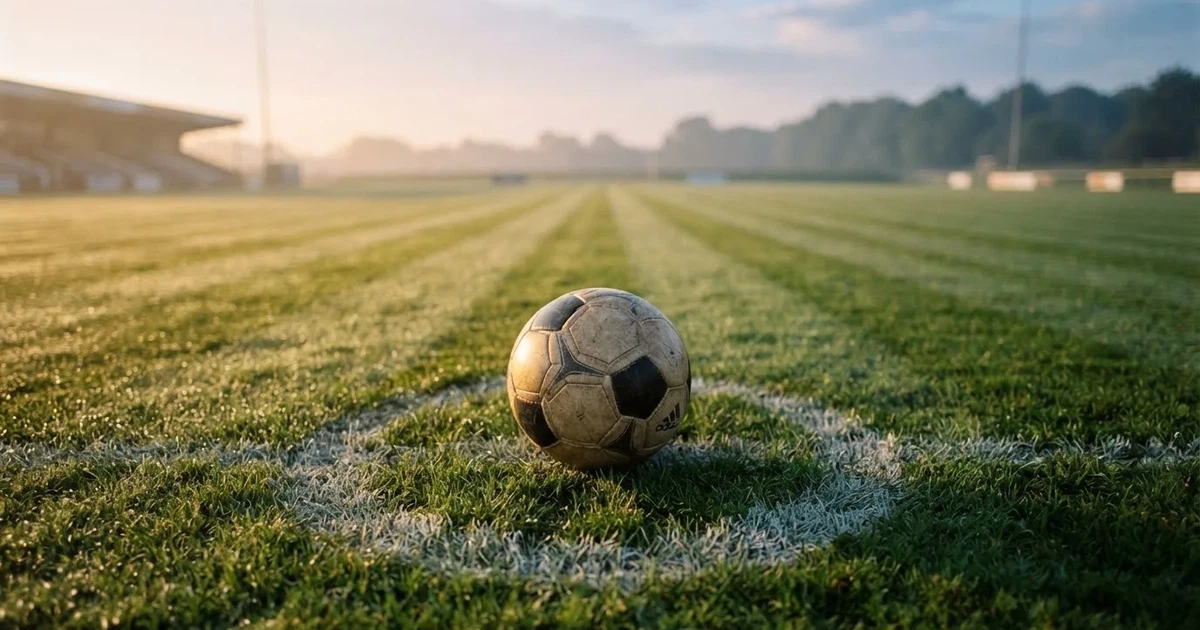 Een voetbal op de middenstip van een grasveld in het ochtendlicht